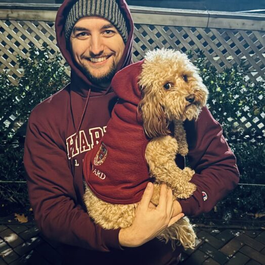 photo of Devin in Harvard hoodie holding a fluffy tan dog