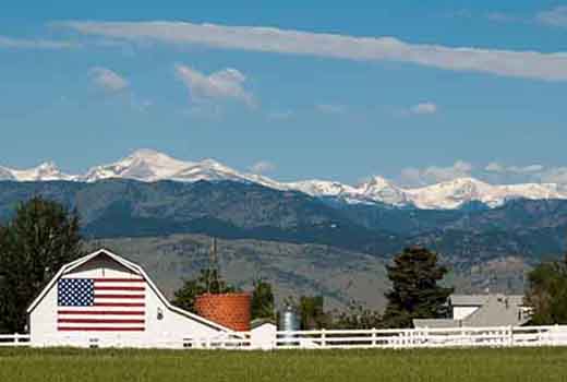 Rural farm with a white barn with a large American flag painted on it.