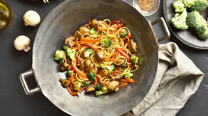 Stir-fry vegetables with noodles in wok pan on dark stone background.